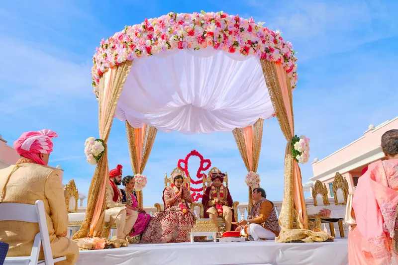 Couple seated under a white and pink floral mandap