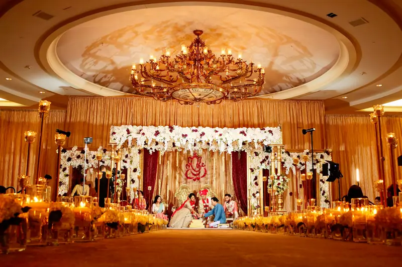 Couple taking pheras under a floral canopy in a chandelier-lit hall